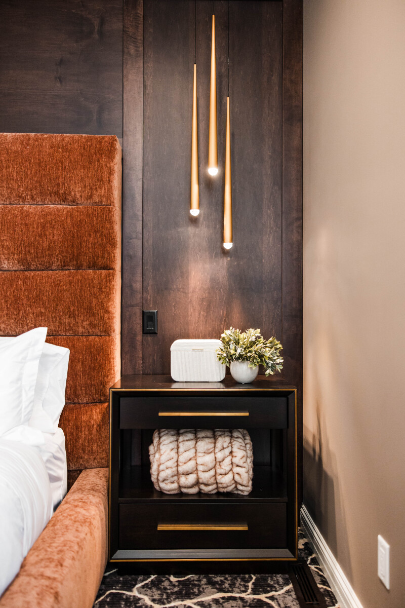 Bedside lights suspended from the ceiling against a dark walnut wall
