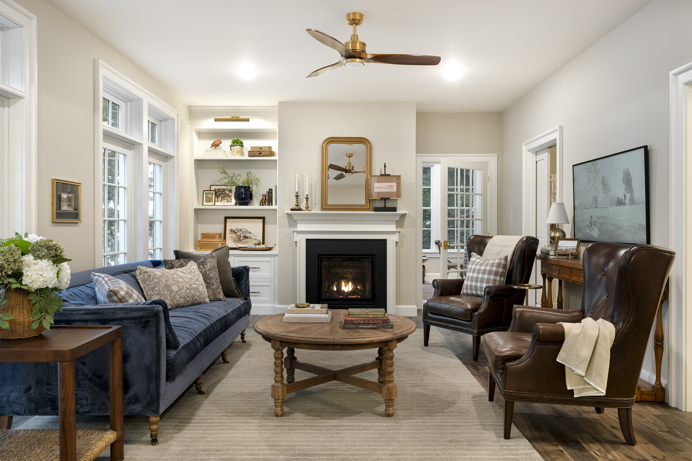 Classic living room with navy velvet sofa, leather wingback chairs, and white fireplace with gilded mirror by Discrete Designs.