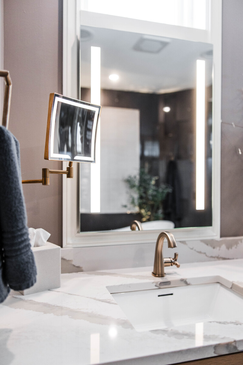 Backlit vanity mirrors with a wall-mounted extending makeup mirror above a custom rift white oak vanity with quartz countertop in a luxury primary bathroom remodel