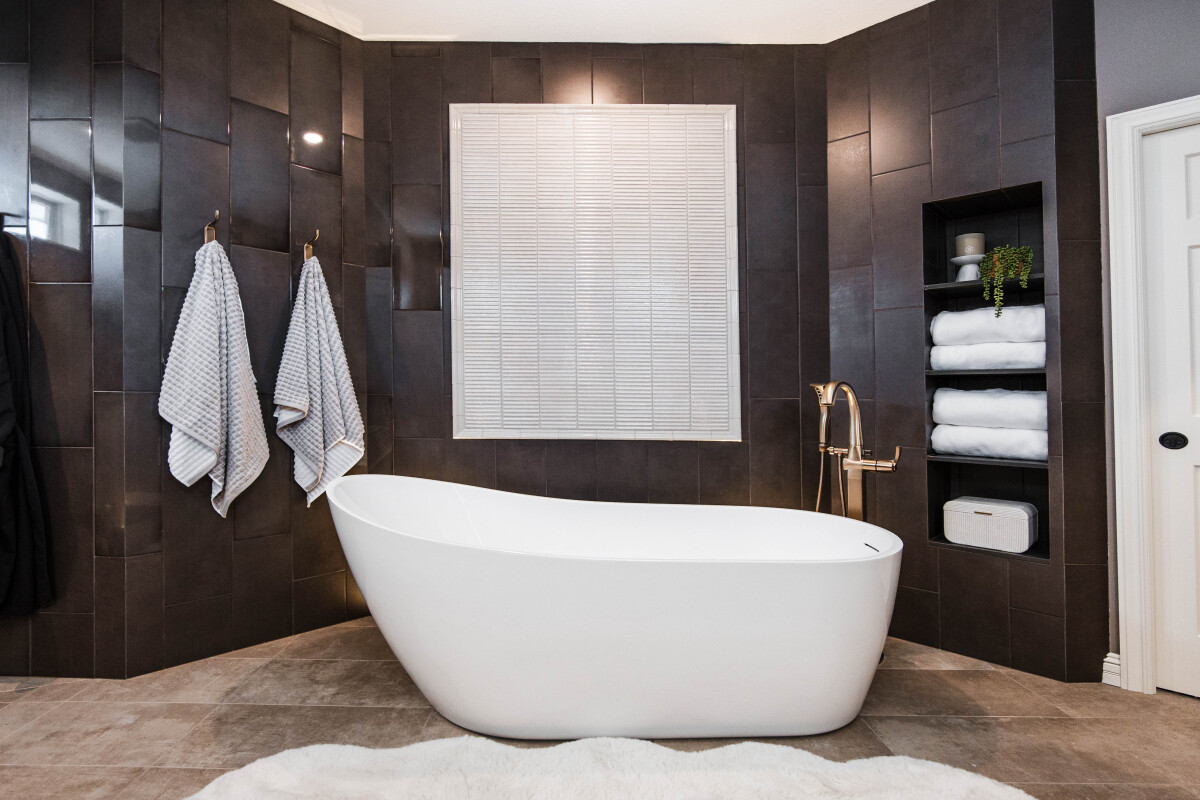 Freestanding white soaking tub against a deep espresso stack-bond tile wall in a spa-inspired primary bathroom remodel. 
