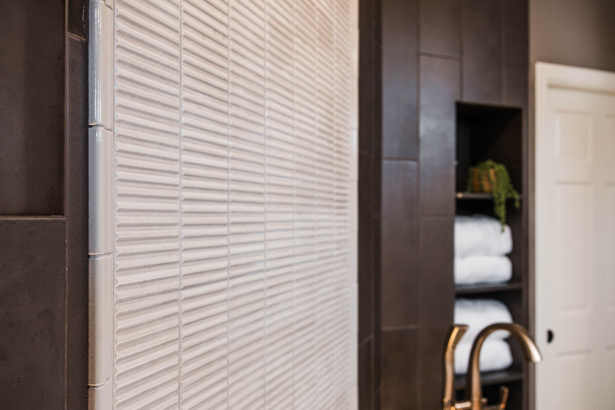 Picture-frame tile detail in a moody primary bathroom, framing the freestanding tub against a wall of variegated dark tile.