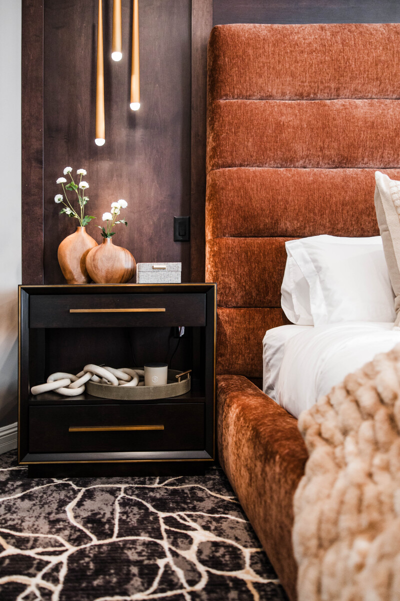 Primary bedroom with rust velvet channel-tufted bed and walnut paneled feature wall and statement bedside lighting